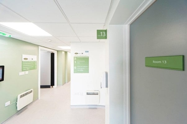 hospital corridor with green signs saying room 13 to show how interior design can have a positive influence towards morale in healthcare buildings